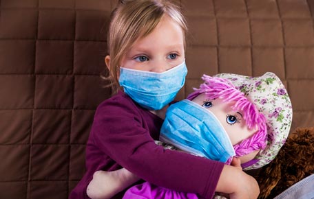 A child with a face mask holding a doll that is also wearing a face mask.