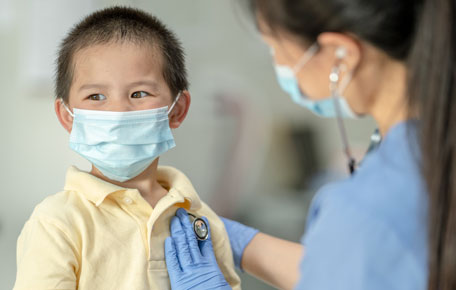 A doctor with face mask checking the heartbeat of a boy.