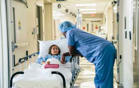 A surgeon in blue scrubs comforts a child on a surgical bed