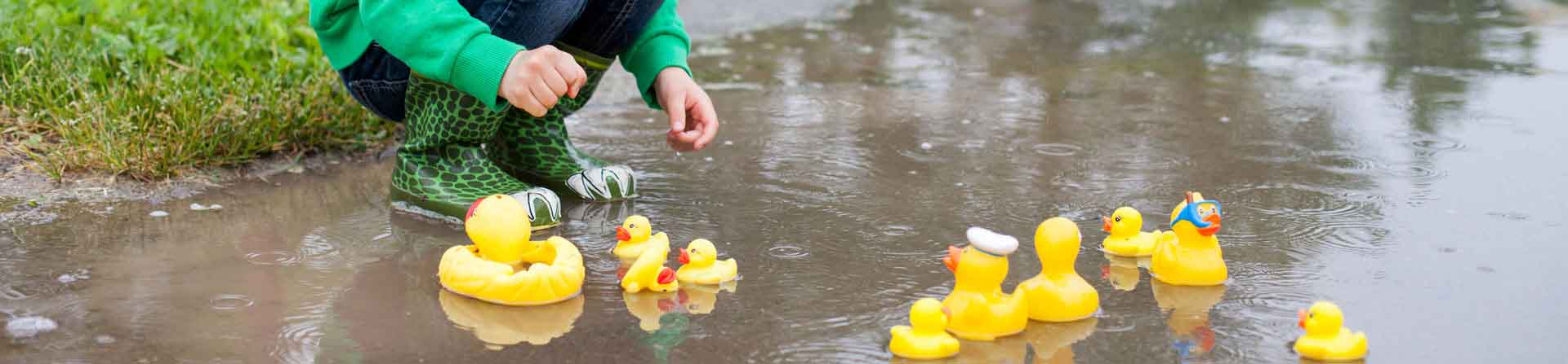 young child playing with rubber ducks in a puddle