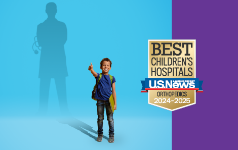 little boy stands in front of blue background with doctor silhouette on wall and best orthopedic children's hospital badge