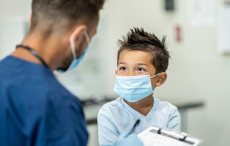 A doctor with a face mask talking to a boy with a face mask.