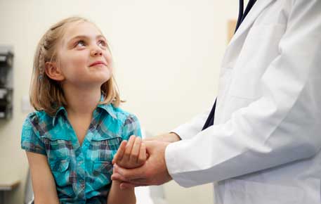 A young girl looking up at a healthcare provider who is holding her hand.
