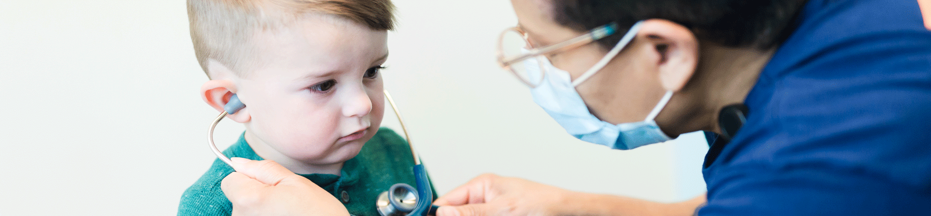 A healthcare provider letting a young boy listen to his own heart with a stethoscope.