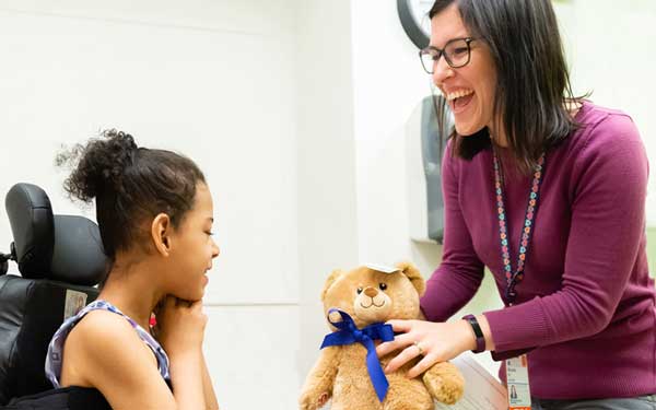 doctor holds teddy bear out to little girl