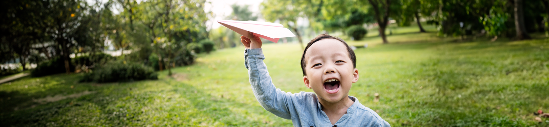 Boy plays with a paper airplane in front of a sunny open field