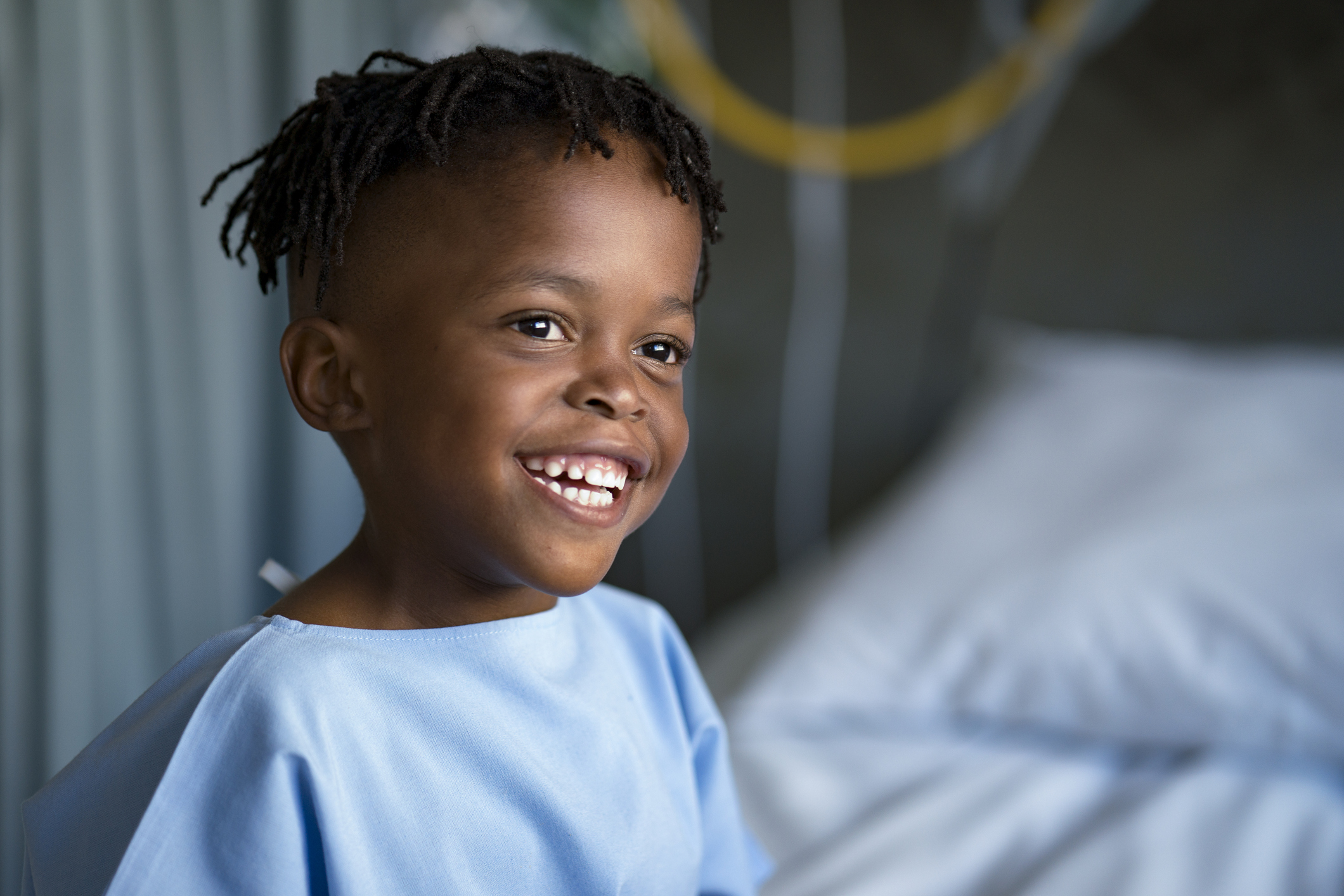 young boy in hospital gown smiles, ready for medical procedure